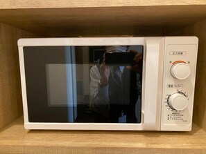 A white microwave with a digital display and control panel, placed on a wooden shelf. - Flexstay Inn Sakuragicho (Yokohama)