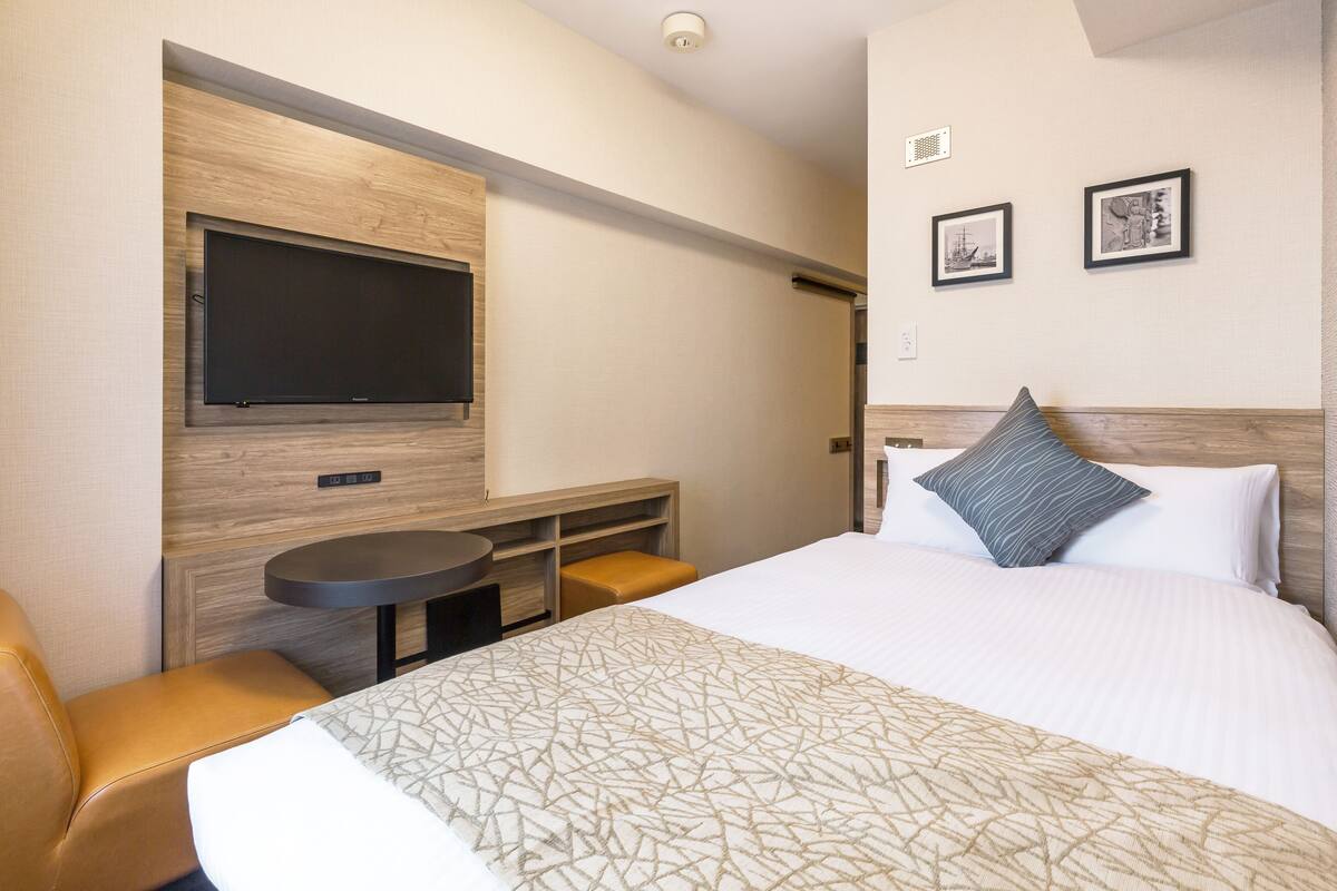 Ein Hotelzimmer mit einem großen Bett, einem flachbildfernseher an der Wand, einem kleinen runden Tisch und einer Sitzecke mit einem Sessel.