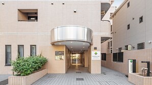 A building entrance with a tiled facade, a central circular structure, and a sign for FlexStay Inn. - Flexstay Inn Sakuragicho (Yokohama)