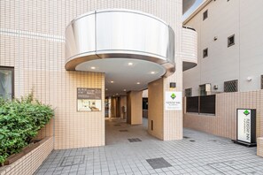 A modern building with a curved metallic entrance, tiled walls, and a sign for FLEXSTAY INN. - Flexstay Inn Sakuragicho (Yokohama)