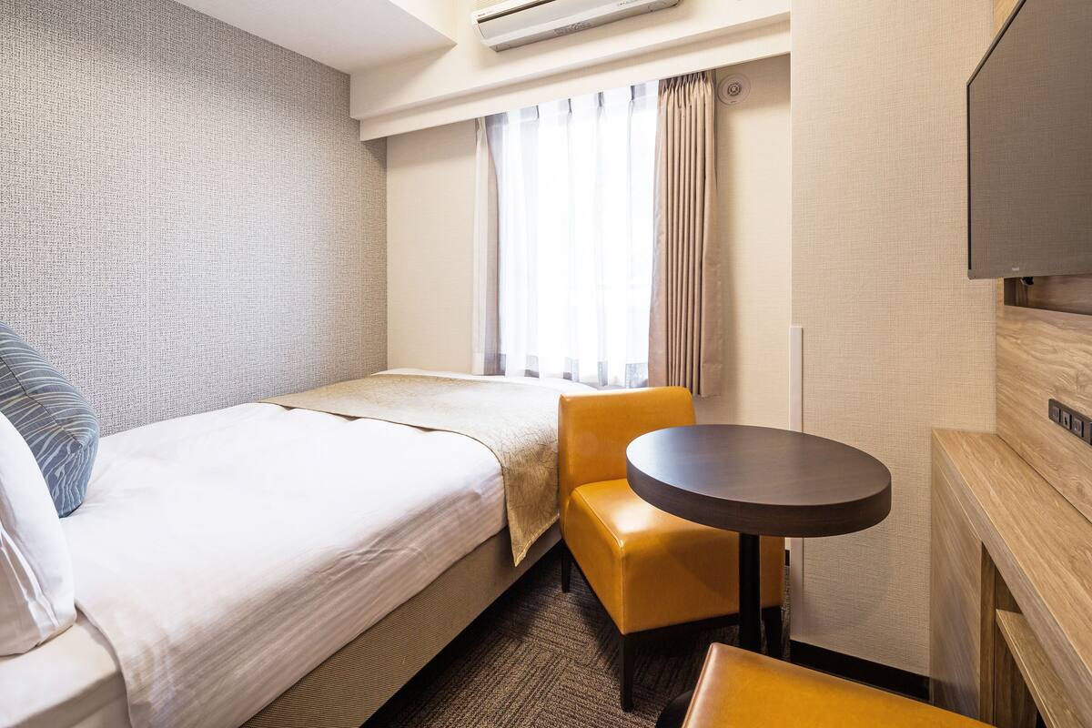 Ein Hotelzimmer mit Bett, kleinem Tisch, Stuhl und Fernseher.