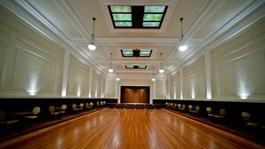 Un salón de conferencias amplio con suelo de madera brillante, paredes blancas y un escenario al frente.