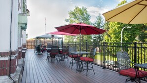 Una terraza de madera con mobiliario exterior, mesas y sillas, y sombrillas rojas que dan sombra.