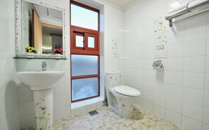 Un baño con azulejos blancos, un ventanal con marco de madera, un lavabo y un inodoro.