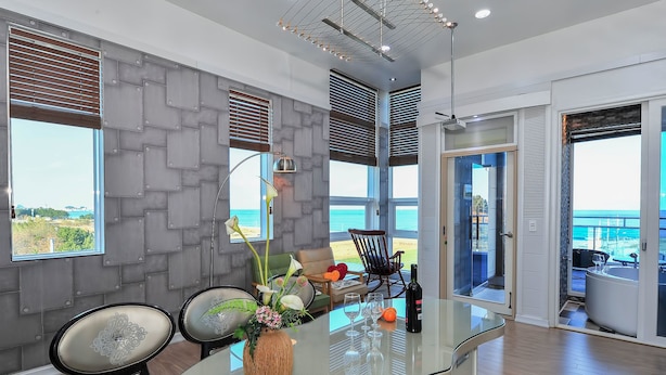 A modern interior with a glass table, chairs, a vase with flowers, and a view of the ocean through large windows. - Sokcho Esher House Pension (Sokcho)
