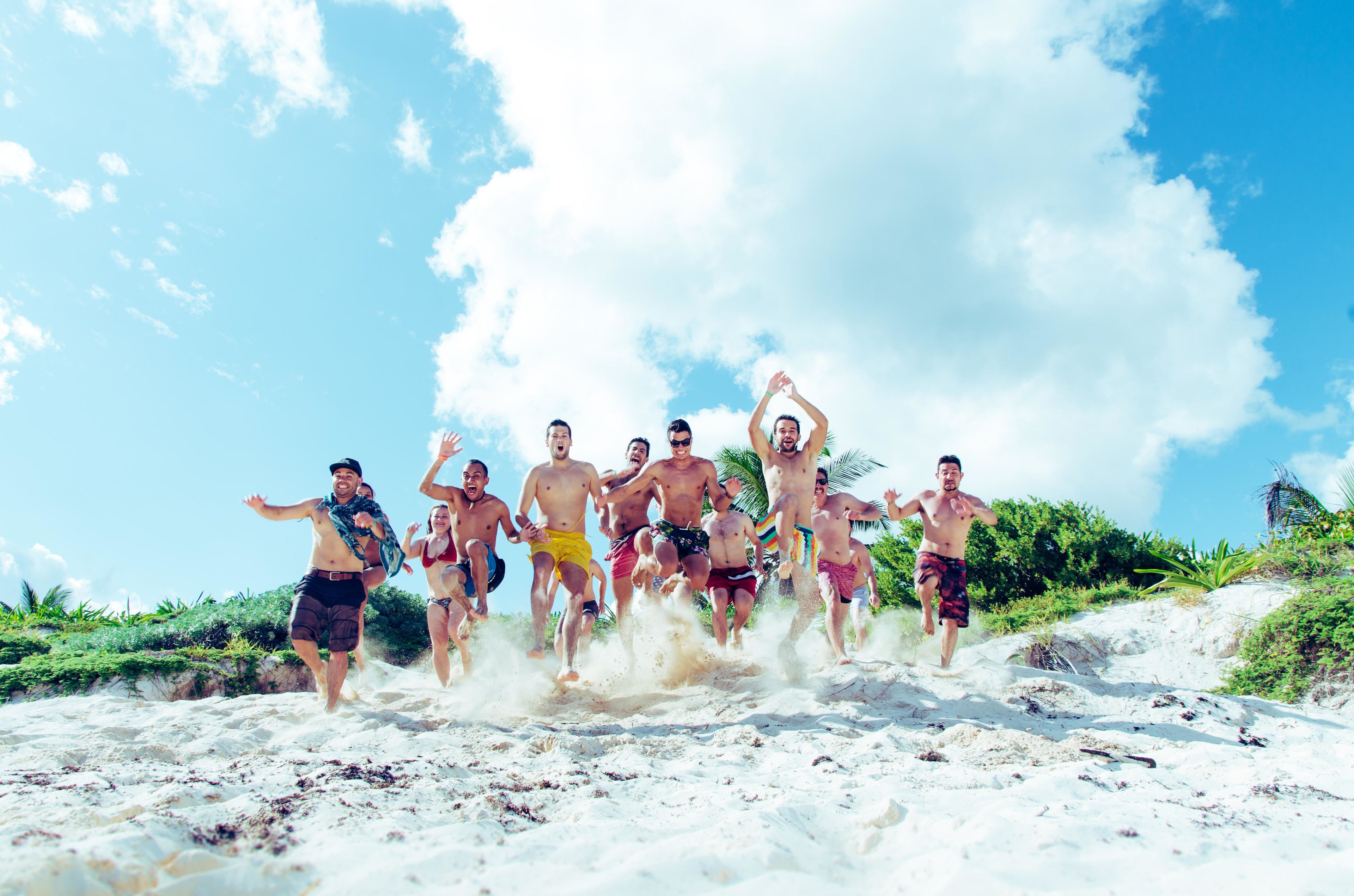 A group of people running on a sandy beach with palm trees and a clear sky in the background.