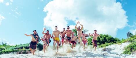 A group of people running on a sandy beach with palm trees and a clear sky in the background.