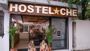 A hostel with a rustic sign reading "HOSTELCHE". Inside, there are two people sitting outside, and the interior features modern furniture and plants. - Che Playa Hostel & Bar (Playa del Carmen)