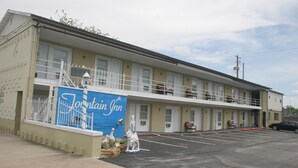 Un motel con letrero azul, asientos exteriores y un estacionamiento.