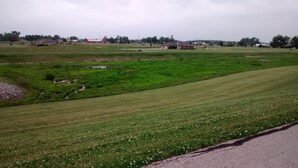 Un paisaje rural con campos verdes, una carretera y edificios a lo lejos.