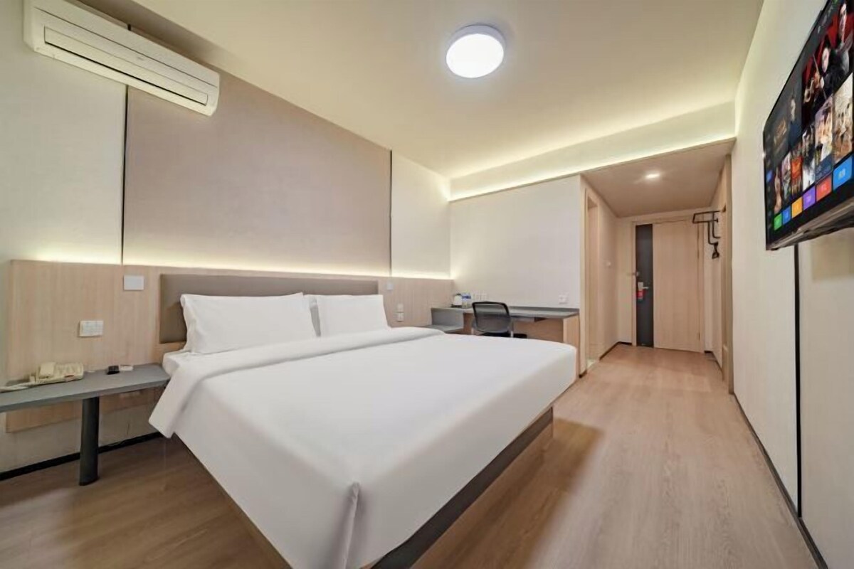 A modern hotel room with a large bed, a desk, and a flat-screen TV mounted on the wall.