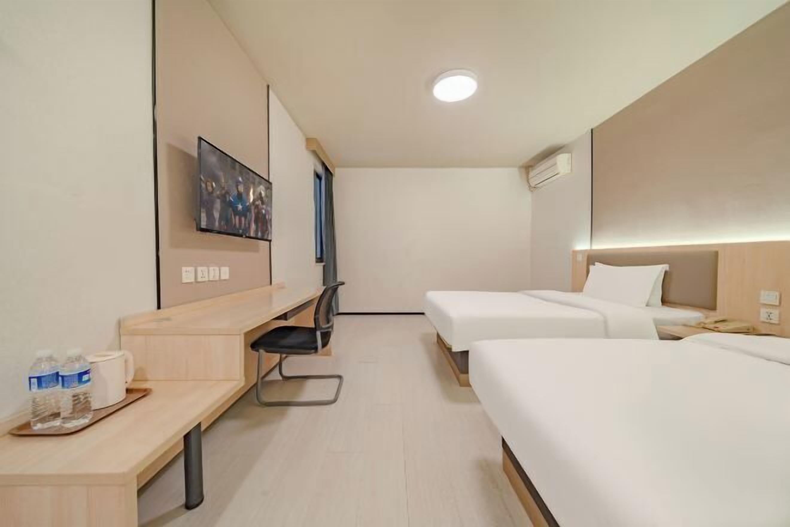 A hotel room with two beds, a desk, a chair, and a TV.