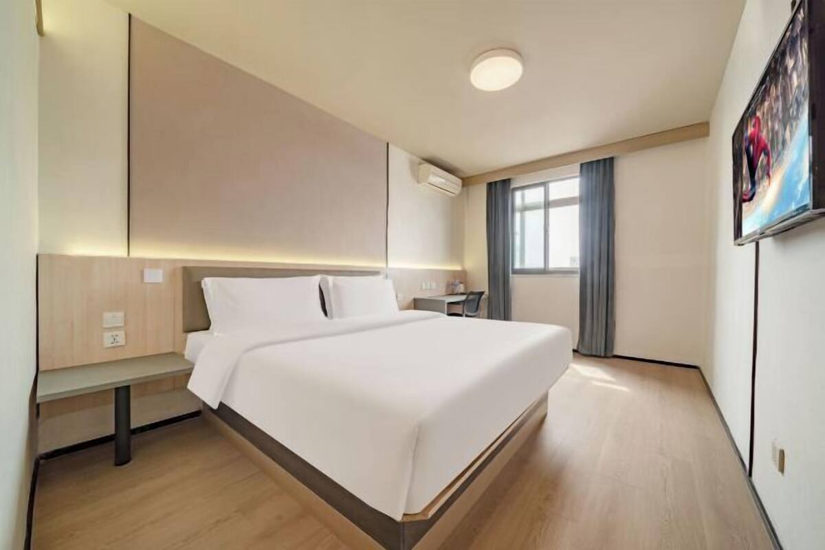 A modern hotel room with a large bed, bedside tables, a desk, and a window with curtains.