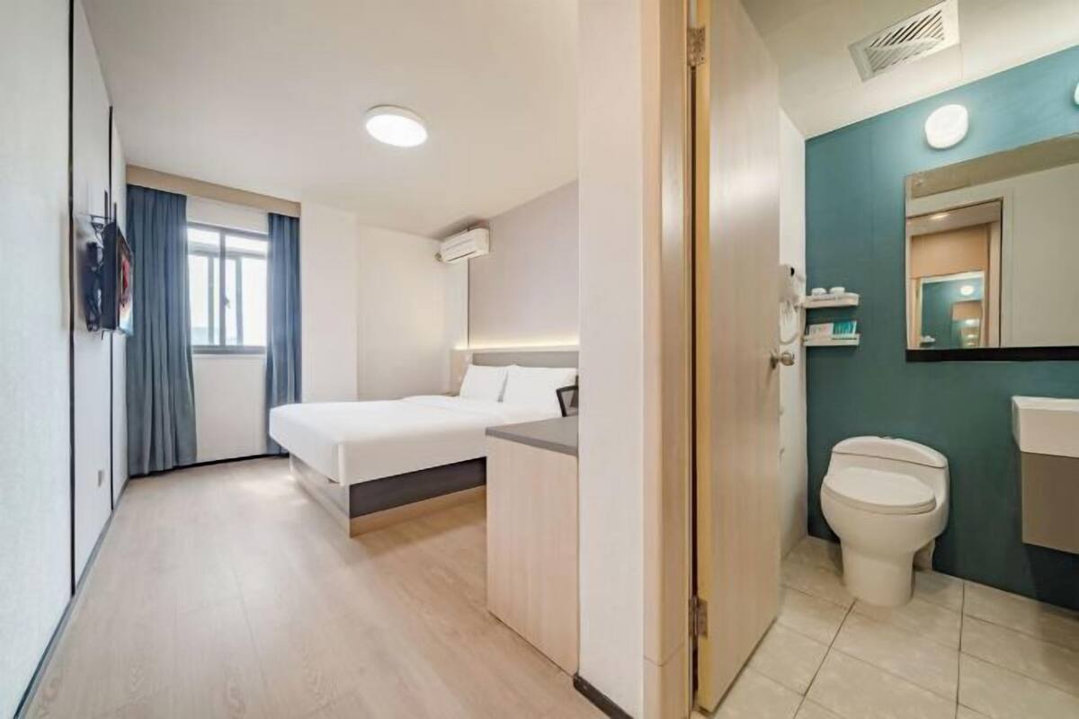 A modern hotel room with a bed, bedside table, and a bathroom with a toilet and sink.