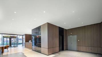 A modern hotel lobby with a glass partition, wooden paneling, and a seating area.