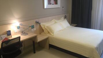 Quarto de hotel com cama, escrivaninha, cadeira e ar condicionado fixado na parede.