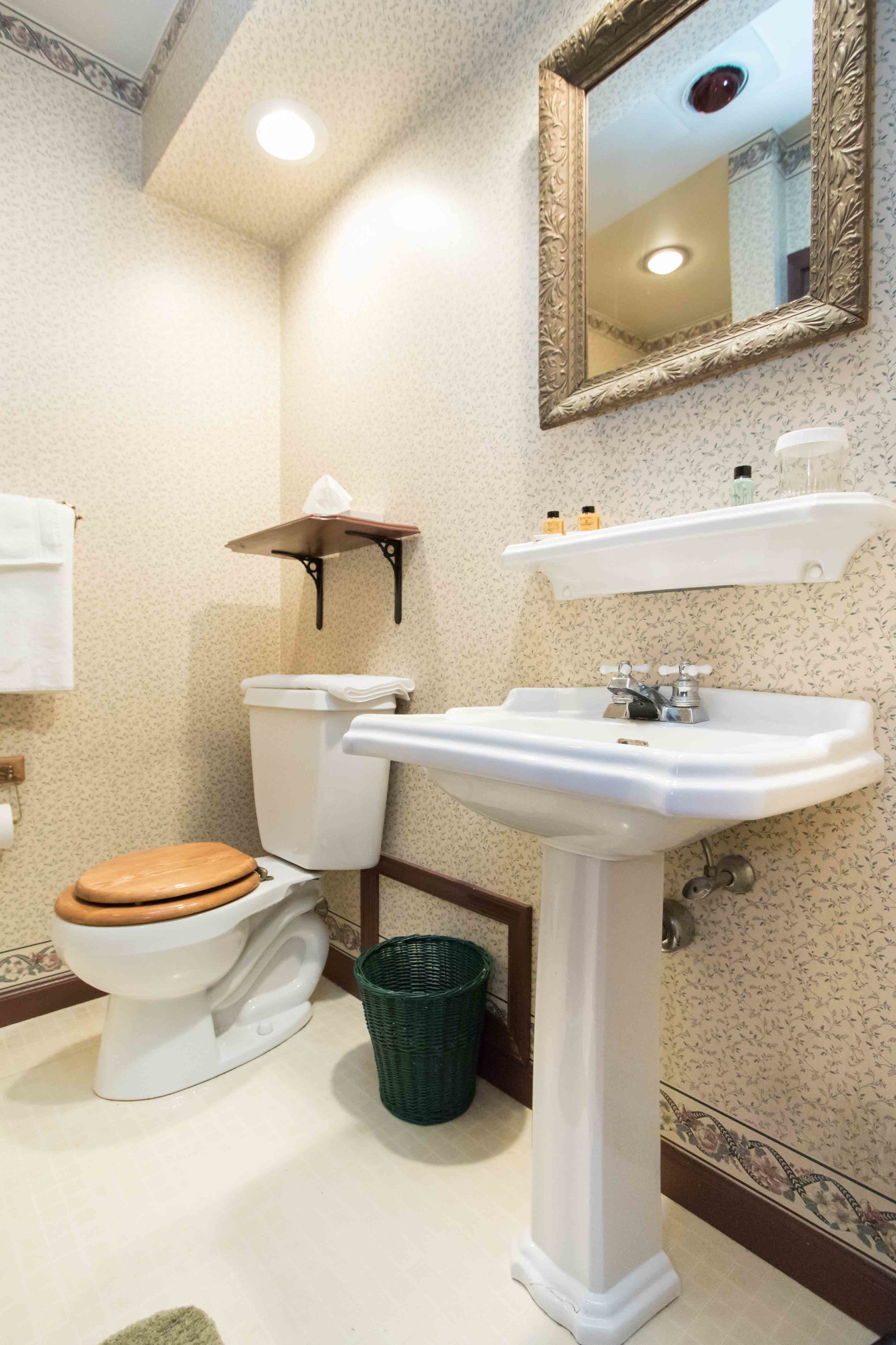 A bathroom with a toilet, sink, mirror, and a trash bin.