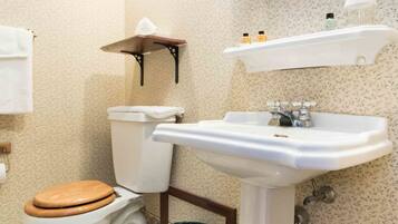 A bathroom with a toilet, sink, mirror, and a trash bin.