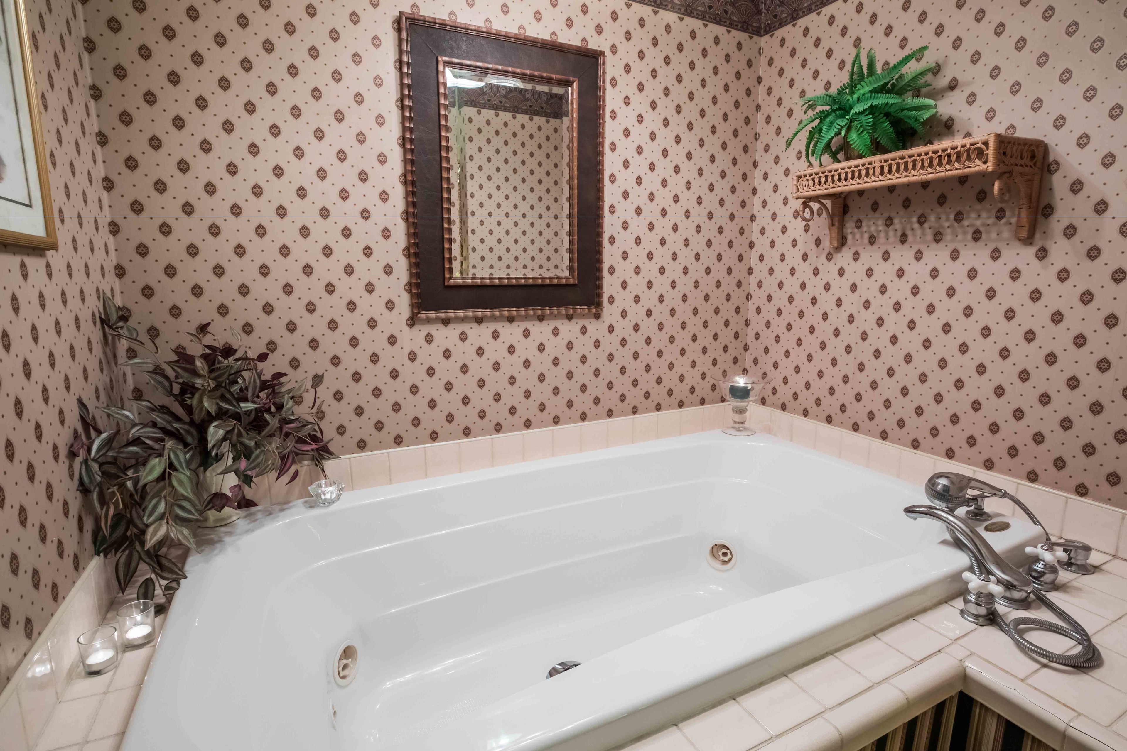 A bathroom with a large bathtub, a mirror, a shelf with a potted plant, and two candles on the floor.