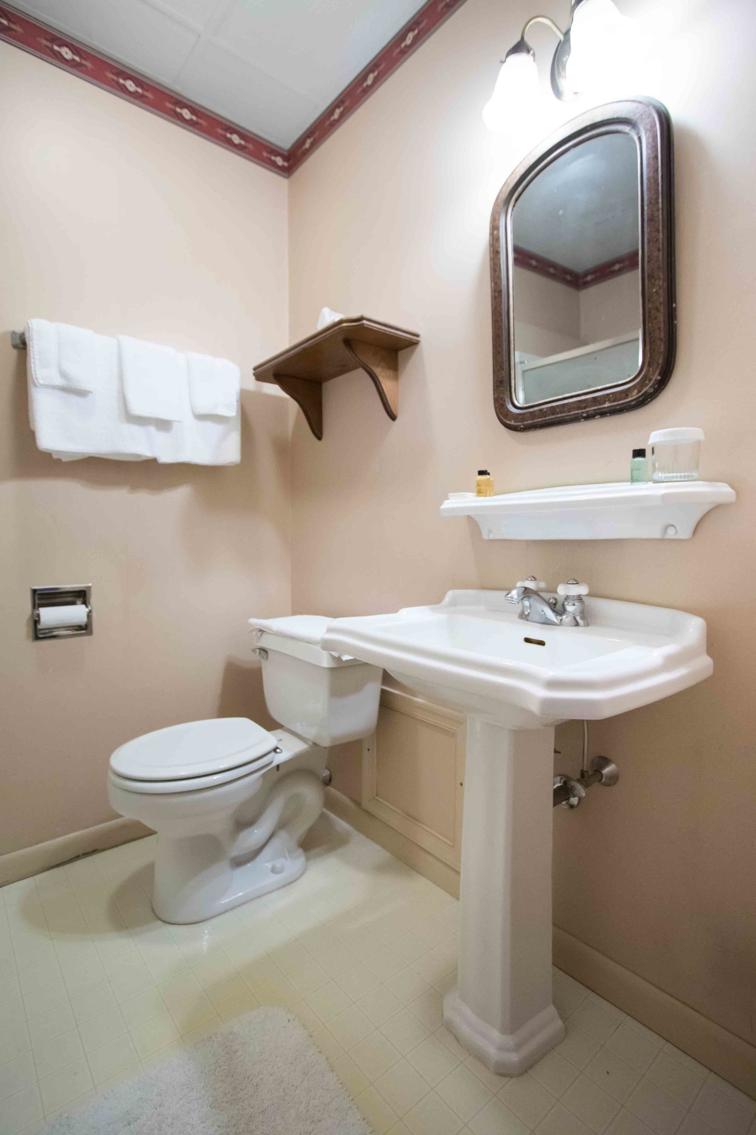 A bathroom with a toilet, sink, mirror, and towel rack.