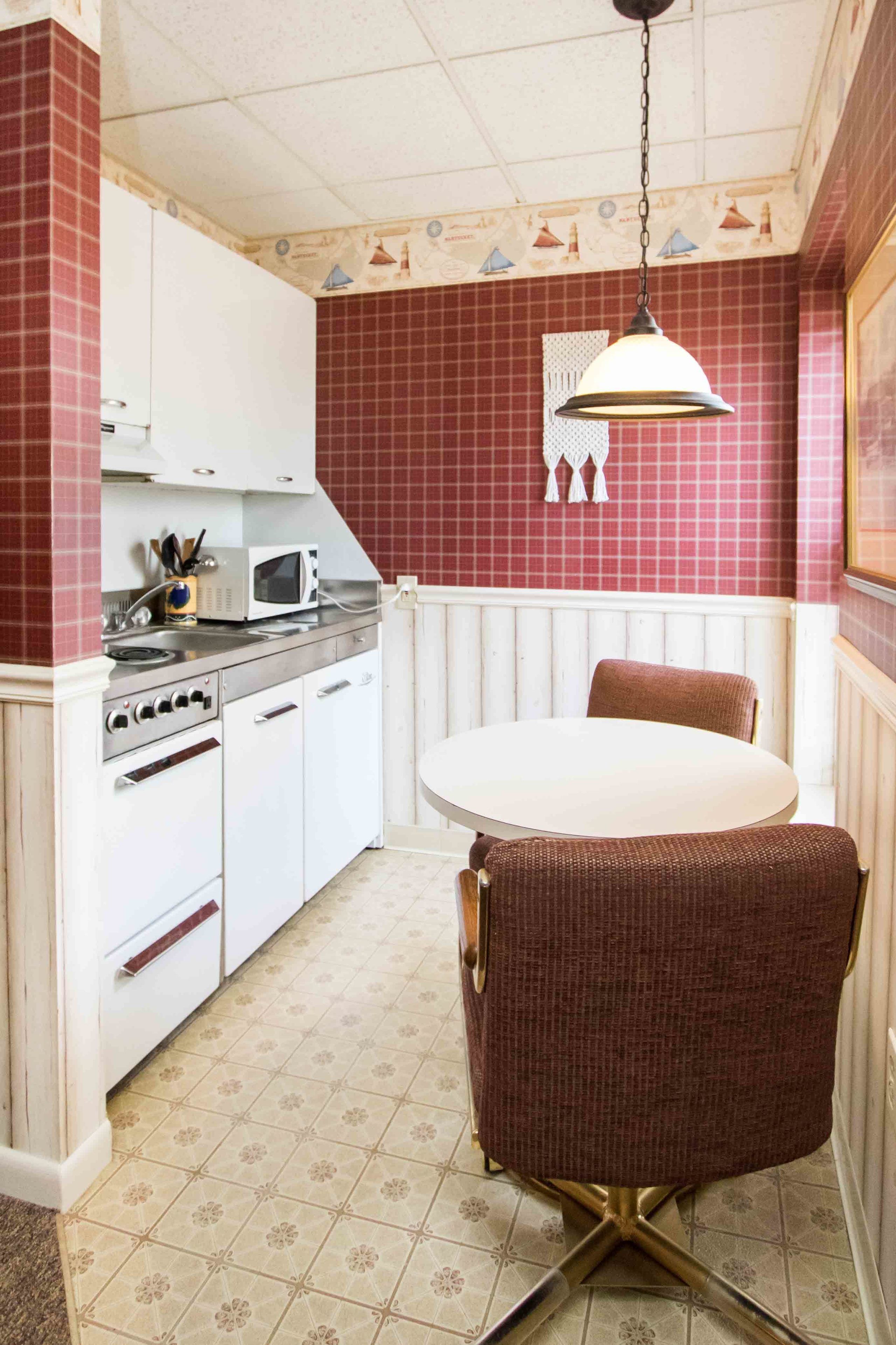 A compact kitchen with white cabinets, a microwave, and a dining table with a single chair.