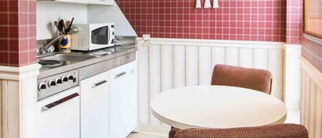 A compact kitchen with white cabinets, a microwave, and a dining table with a single chair.