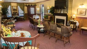 A cozy hotel room with a fireplace, comfortable seating, a television, and a dining area with a table set for two. - The Globe Inn (East Greenville)