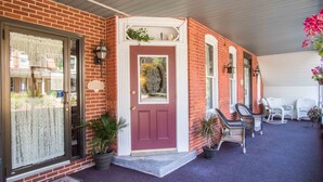 A brick house with a red door, a porch with white chairs, and a small garden area. - The Globe Inn (East Greenville)