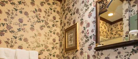 A bathroom with floral wallpaper, a white toilet, a pedestal sink, and a wicker basket.