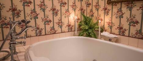 A bathroom with a white bathtub, a shower with a hose, and floral wallpaper.