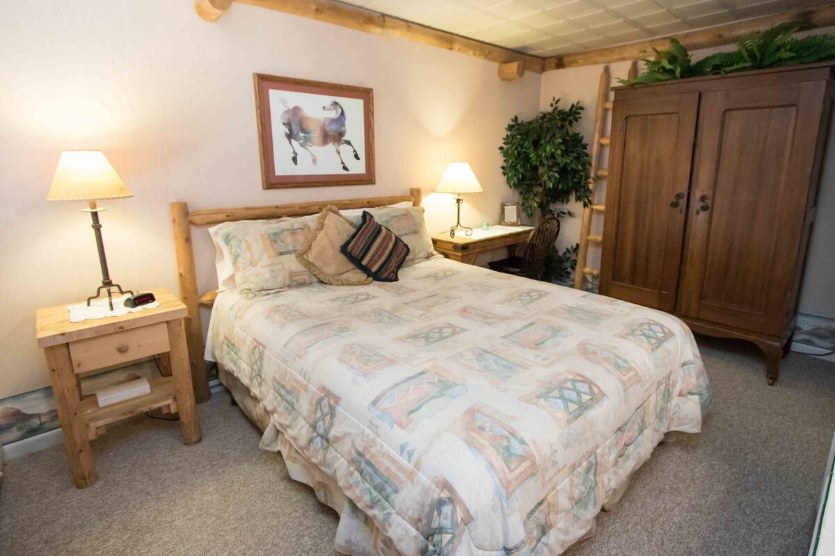 A bedroom with a bed, two bedside tables with lamps, a wooden wardrobe, and a framed picture on the wall.