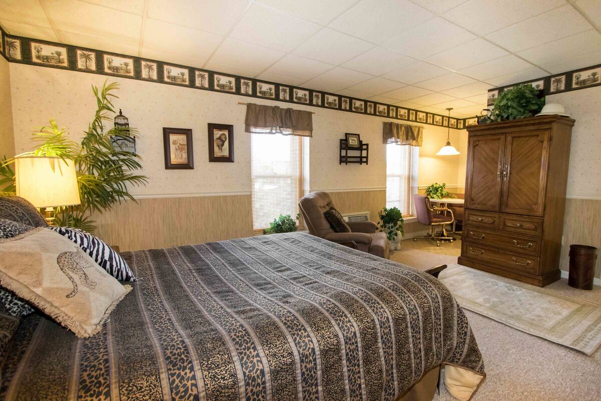 A bedroom with a large bed, a chair, a cabinet, and a desk.