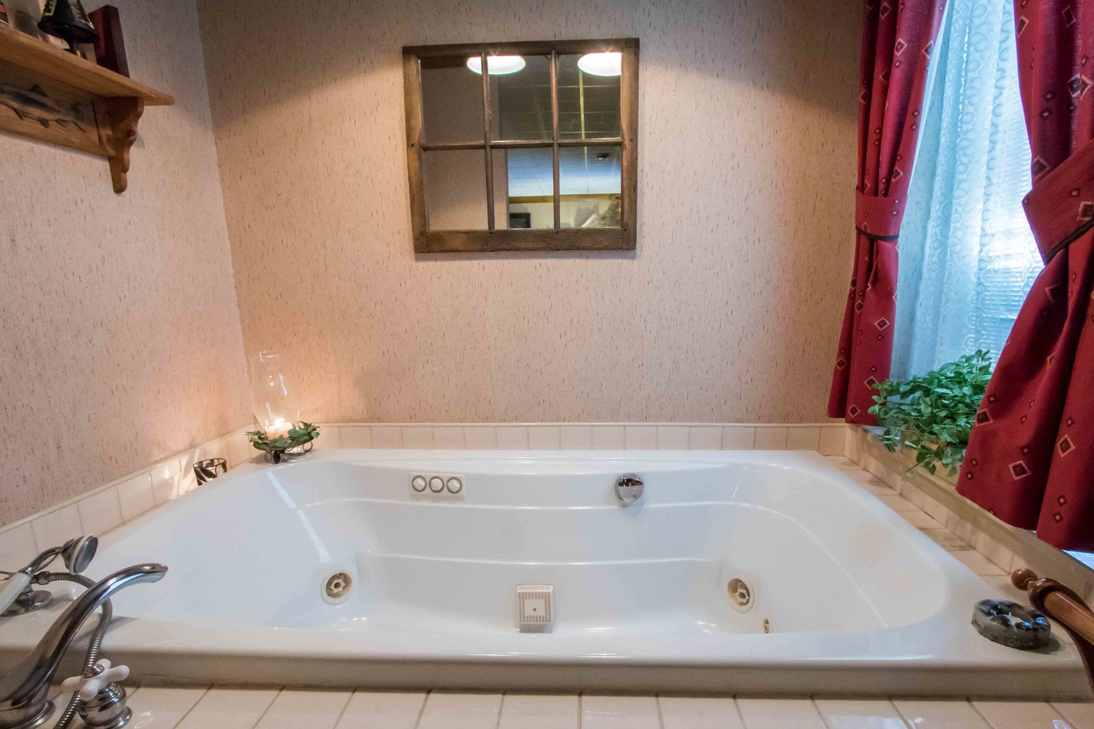 A large bathtub with a window above it, a small shelf with items, and a plant next to the window.
