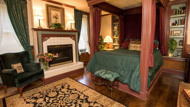 A four-poster canopy bed with a green bedspread, a fireplace with a mantel, a dark green armchair, and a patterned rug. - The Globe Inn (East Greenville)