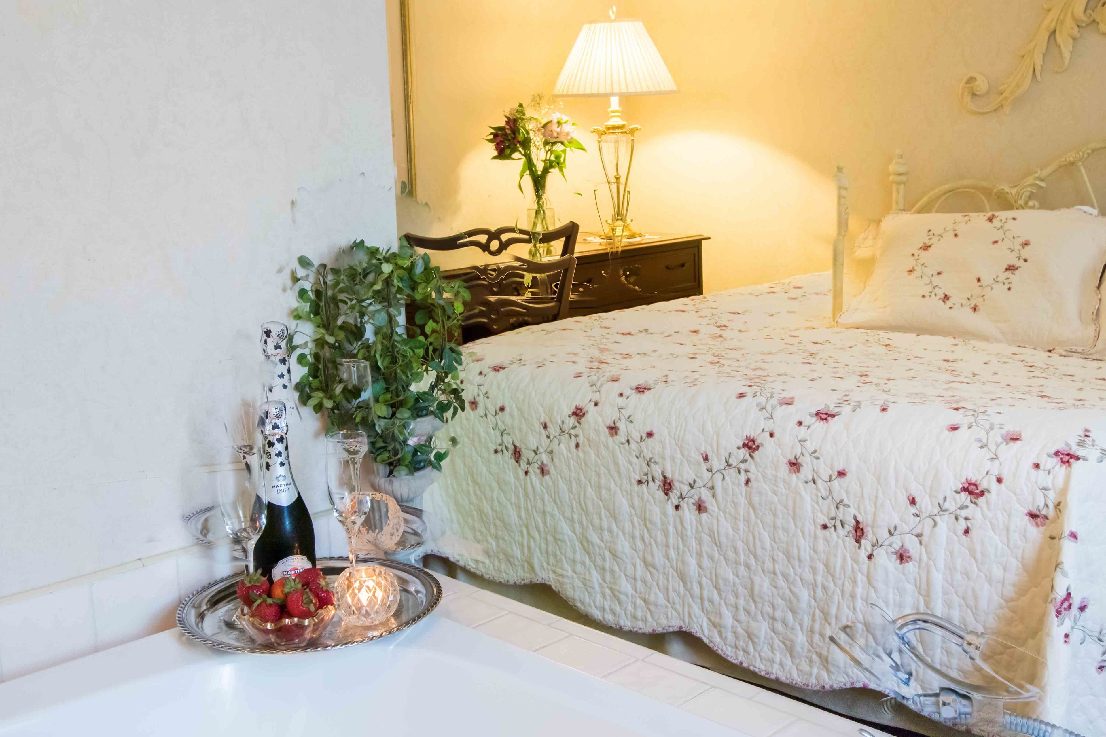 A neatly made bed with a floral bedspread, a bedside lamp, and a decorative vase with flowers.