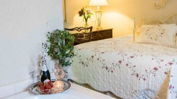 A neatly made bed with a floral bedspread, a bedside lamp, and a decorative vase with flowers.