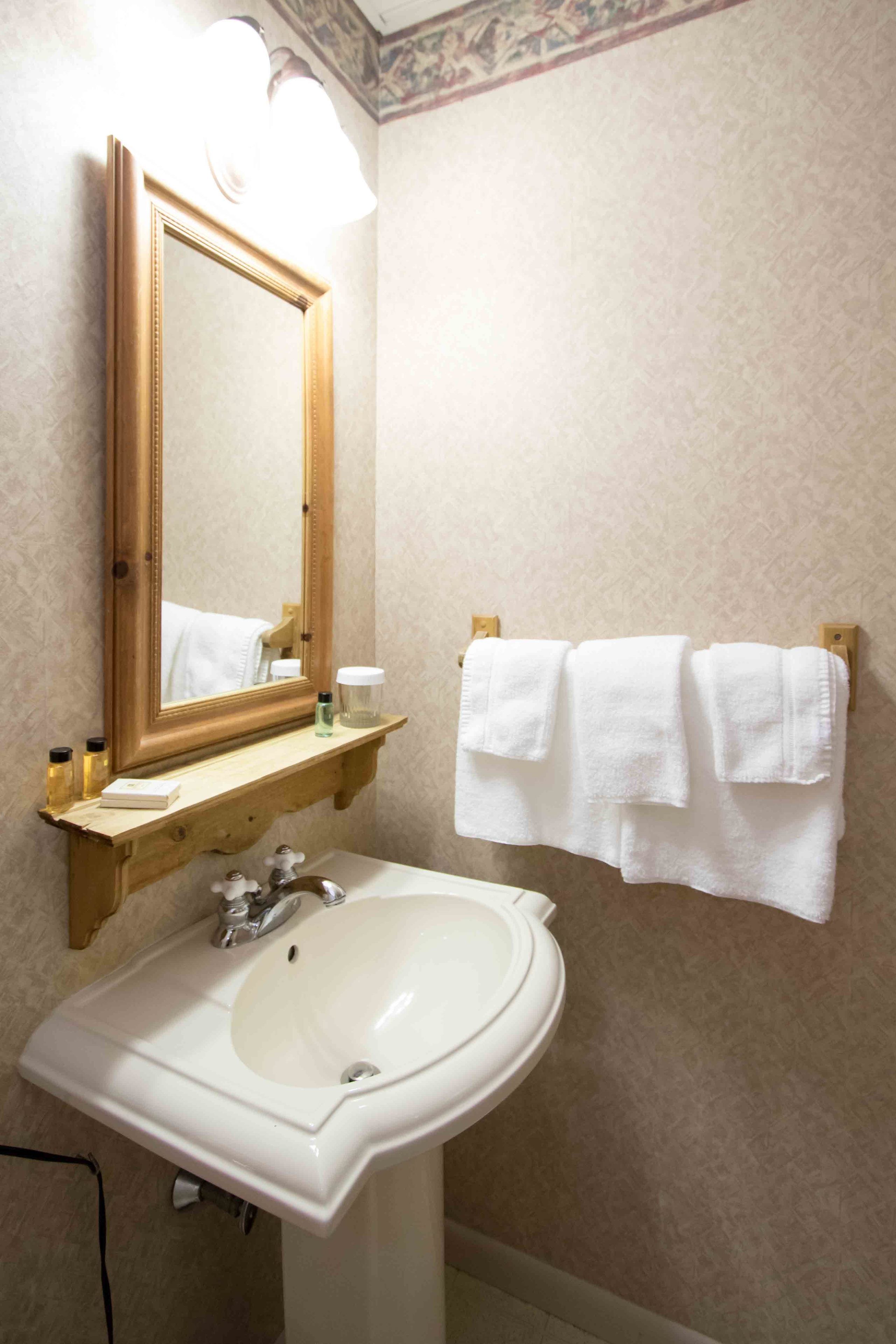 A bathroom with a white sink, a mirror, and a towel rack with white towels.