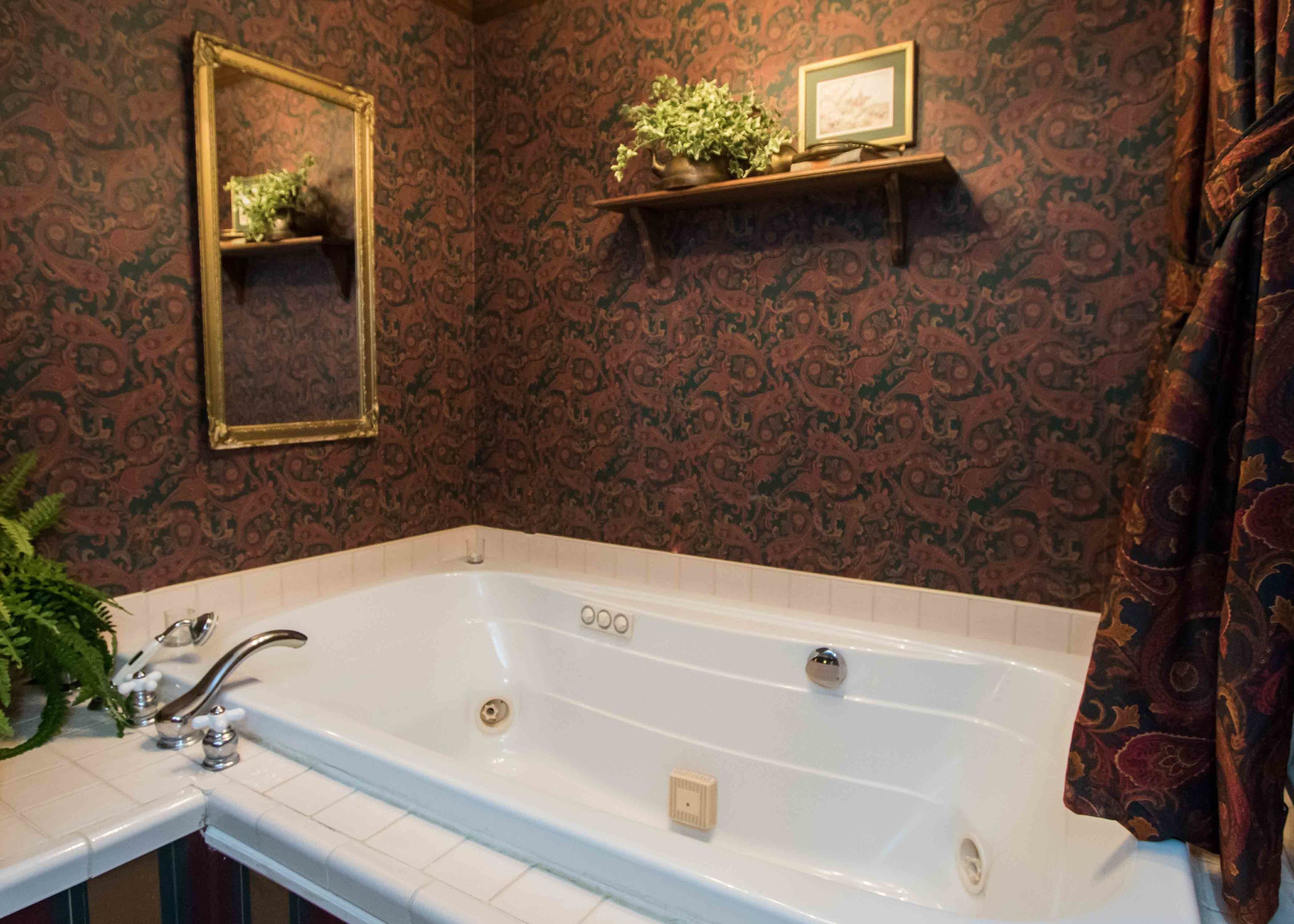 A bathroom with a large white bathtub, a mirror, and a shelf with decorative items.