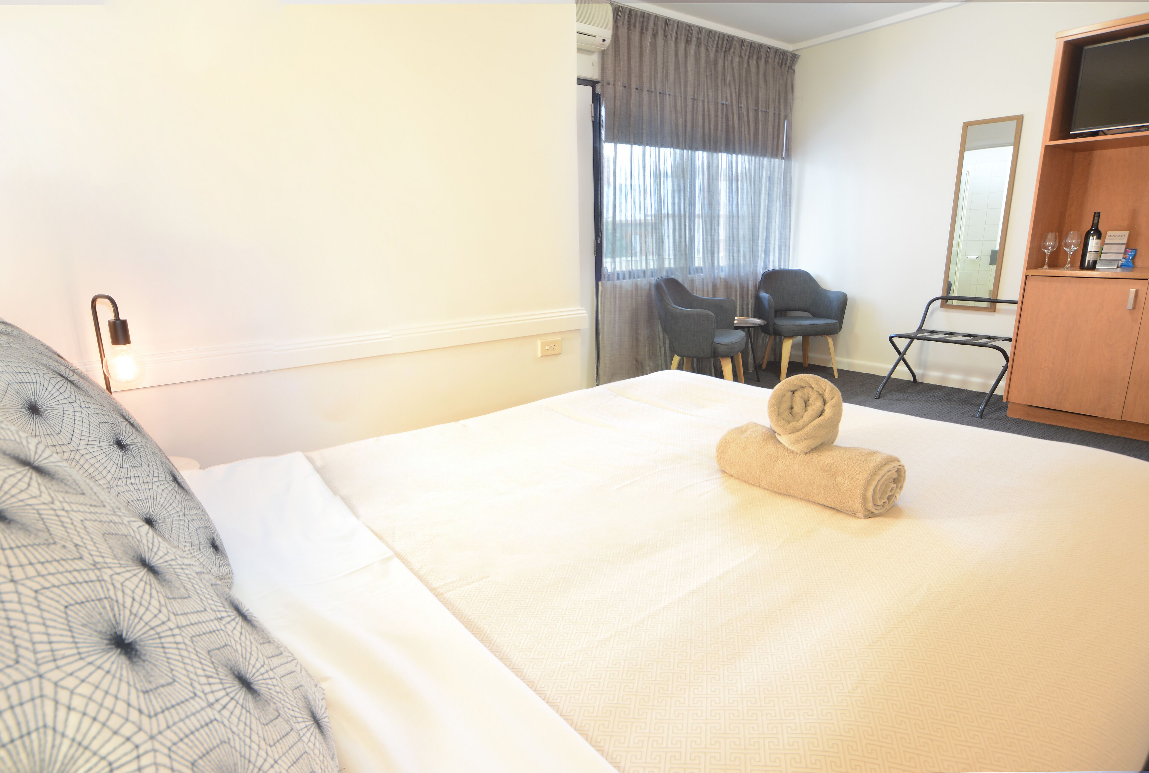 Habitación de hotel con una cama grande, un escritorio, dos sillas, un televisor y un espejo.