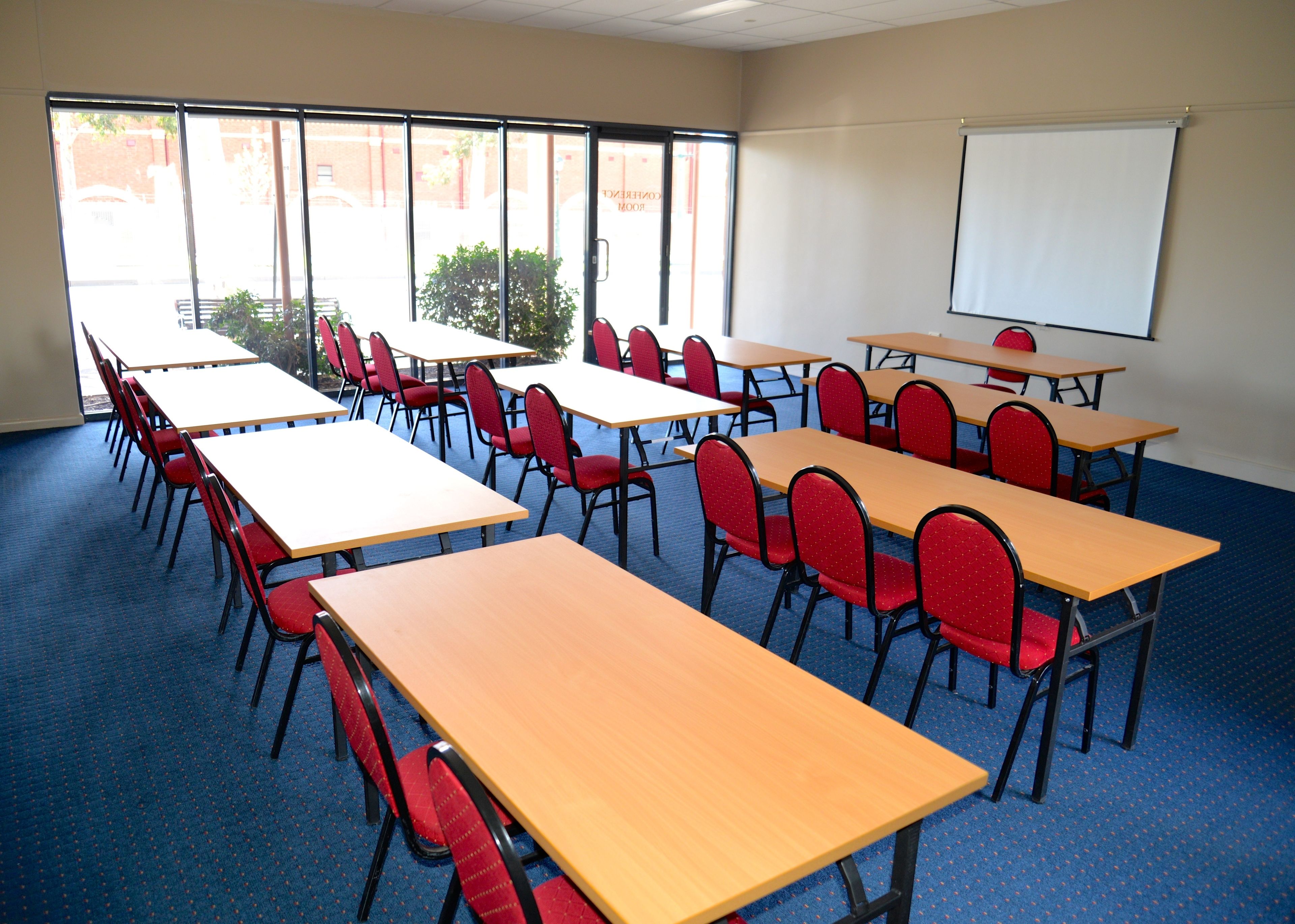 A classroom with rows of desks and chairs, a projector screen, and large windows.