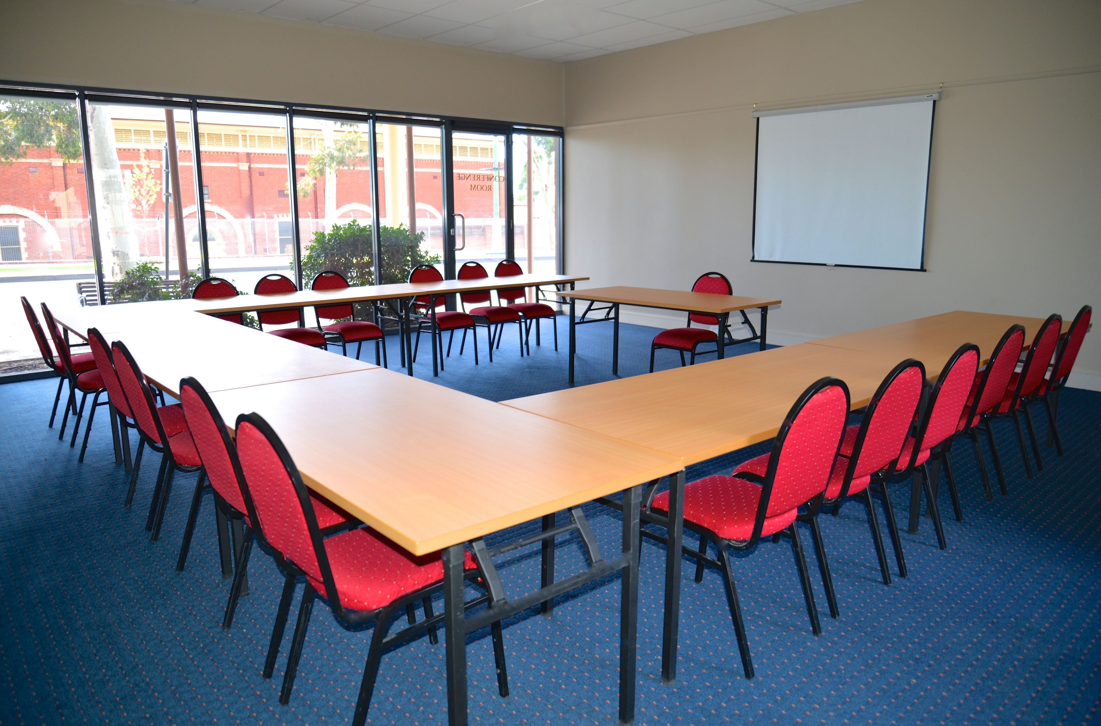 Une salle de conférence avec de longues tables et des chaises rouges, de grandes fenêtres et un tableau blanc.