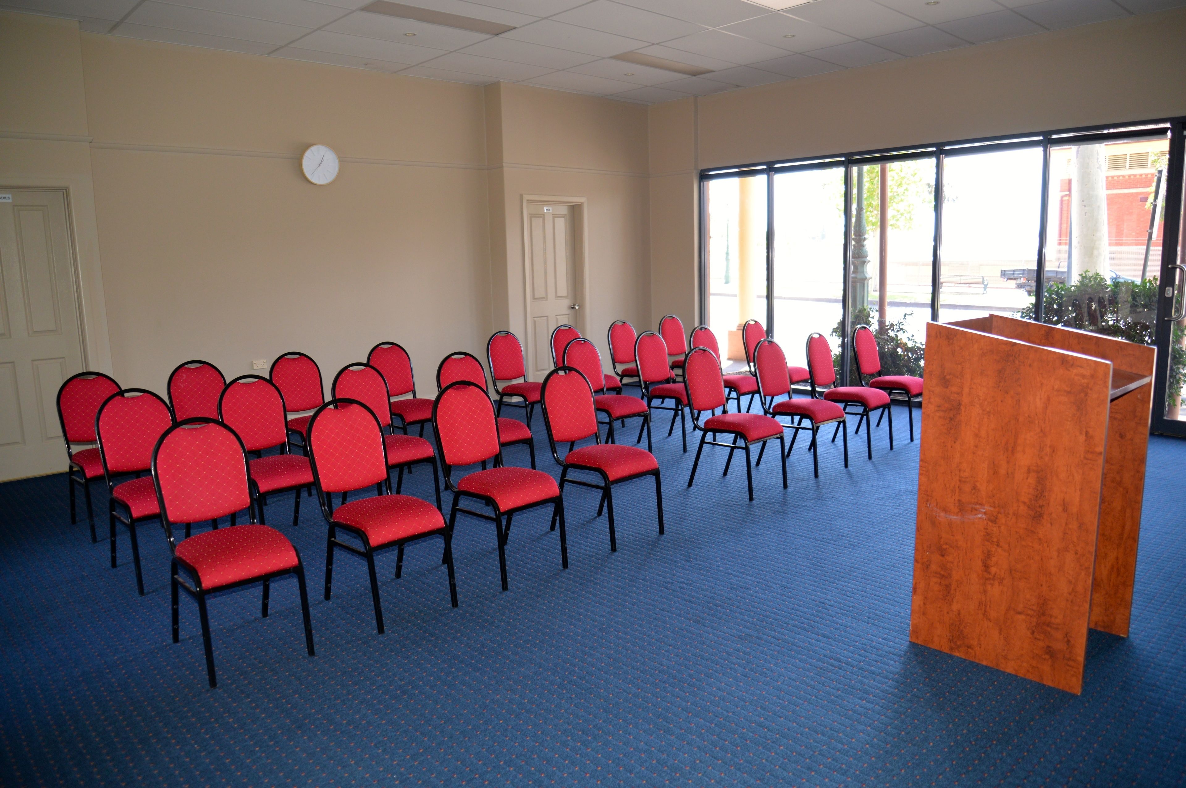 A conference room with rows of red chairs, a podium, and large windows.