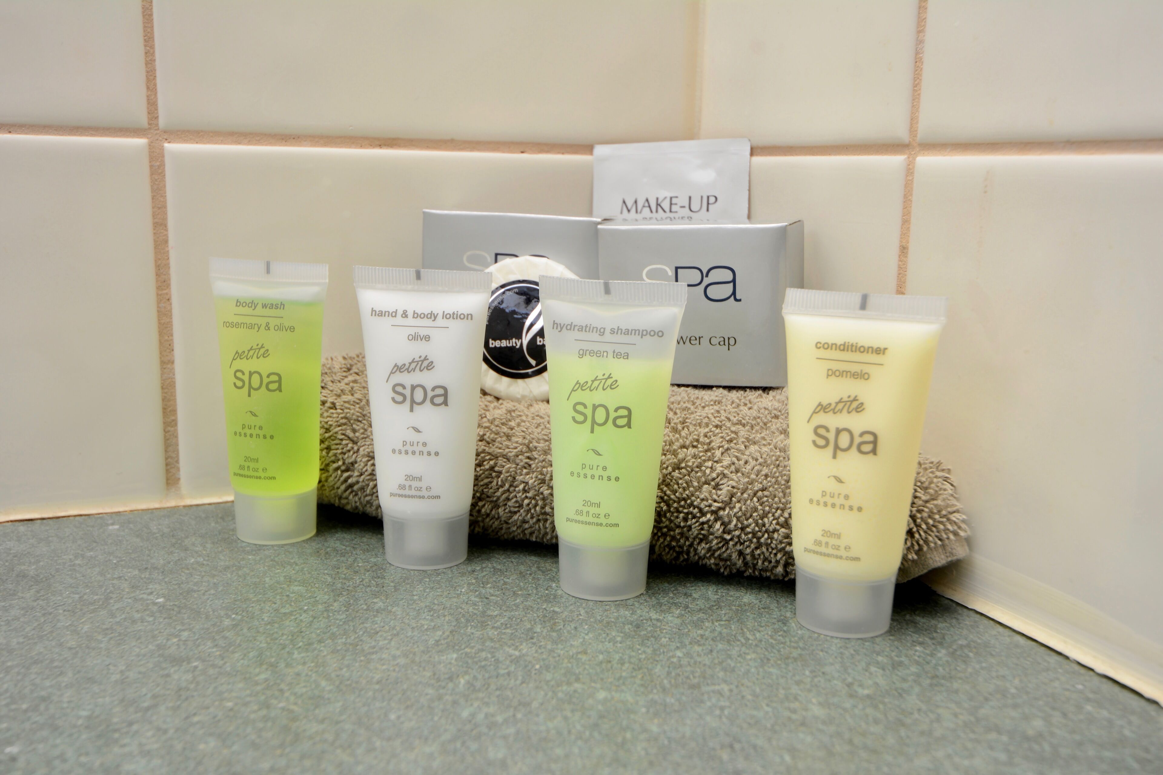 Une sélection de produits de spa, comprenant un gel douche, une lotion pour les mains et le corps, un shampooing hydratant, un bonnet de douche et un après-shampooing, disposés sur une surface carrelée.