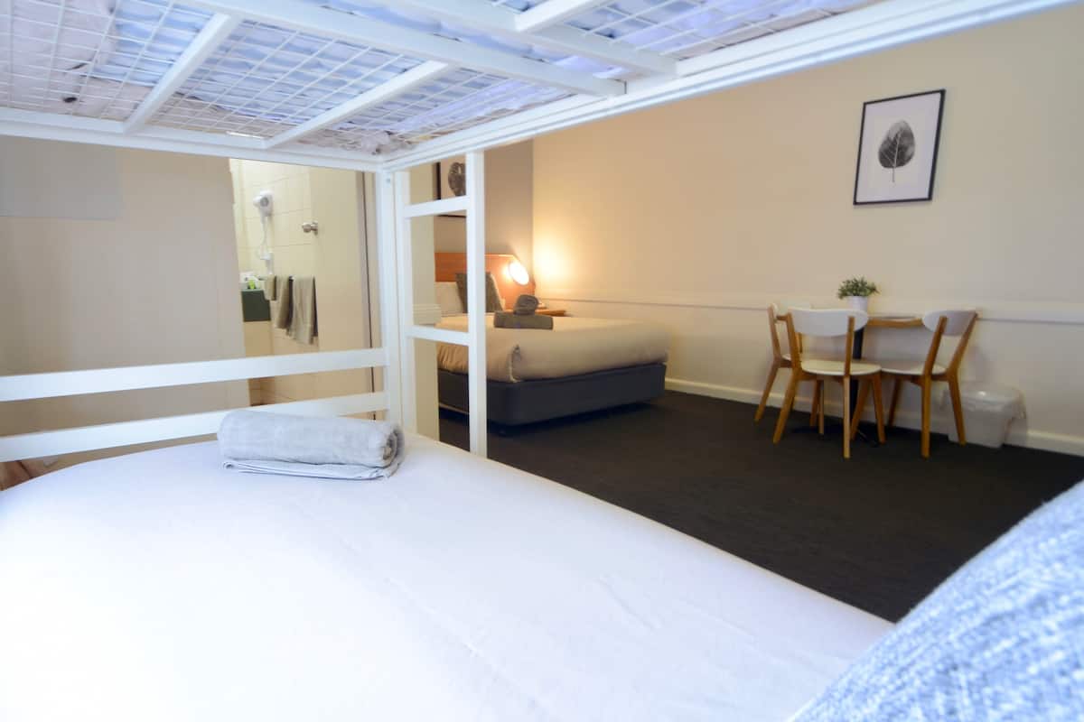 A bedroom with a bed, a desk, and a chair. There is a mirror, a lamp, and a picture on the wall.