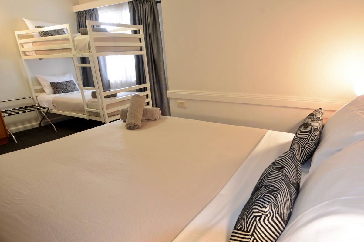 A hotel room with a bunk bed, a single bed, and a small table with a chair.