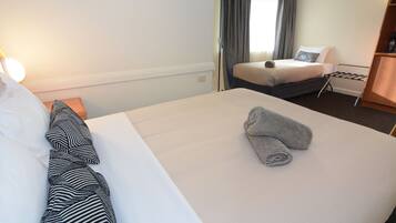 A hotel room with a large bed, a bedside table, a lamp, a window with curtains, and a small seating area with a chair and a table.