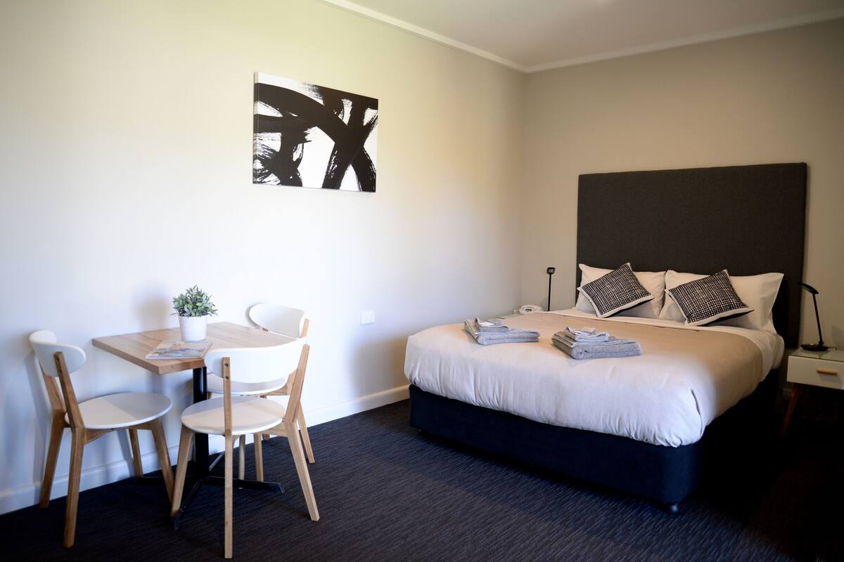 A hotel room with a bed, bedside table, lamp, and a desk with chairs.