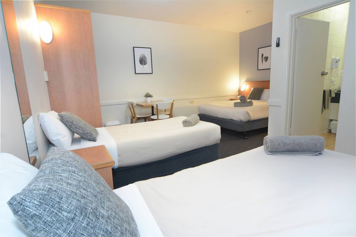 A hotel room with two beds, a desk, and a chair. There are wall-mounted lights and a phone on the wall.