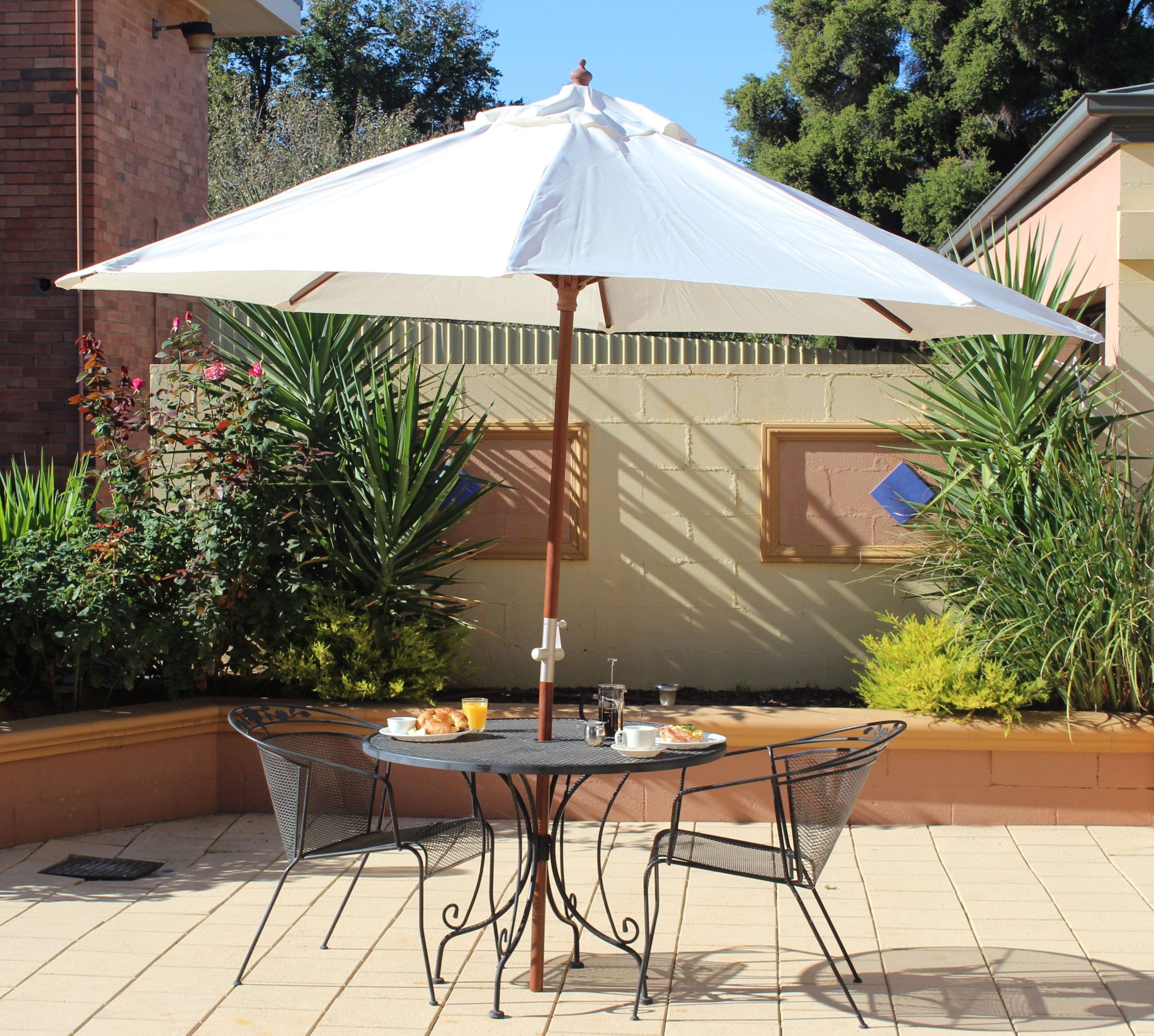 Een terras met een ronde tafel en stoelen, een parasol en een ontbijt met croissants en sap.