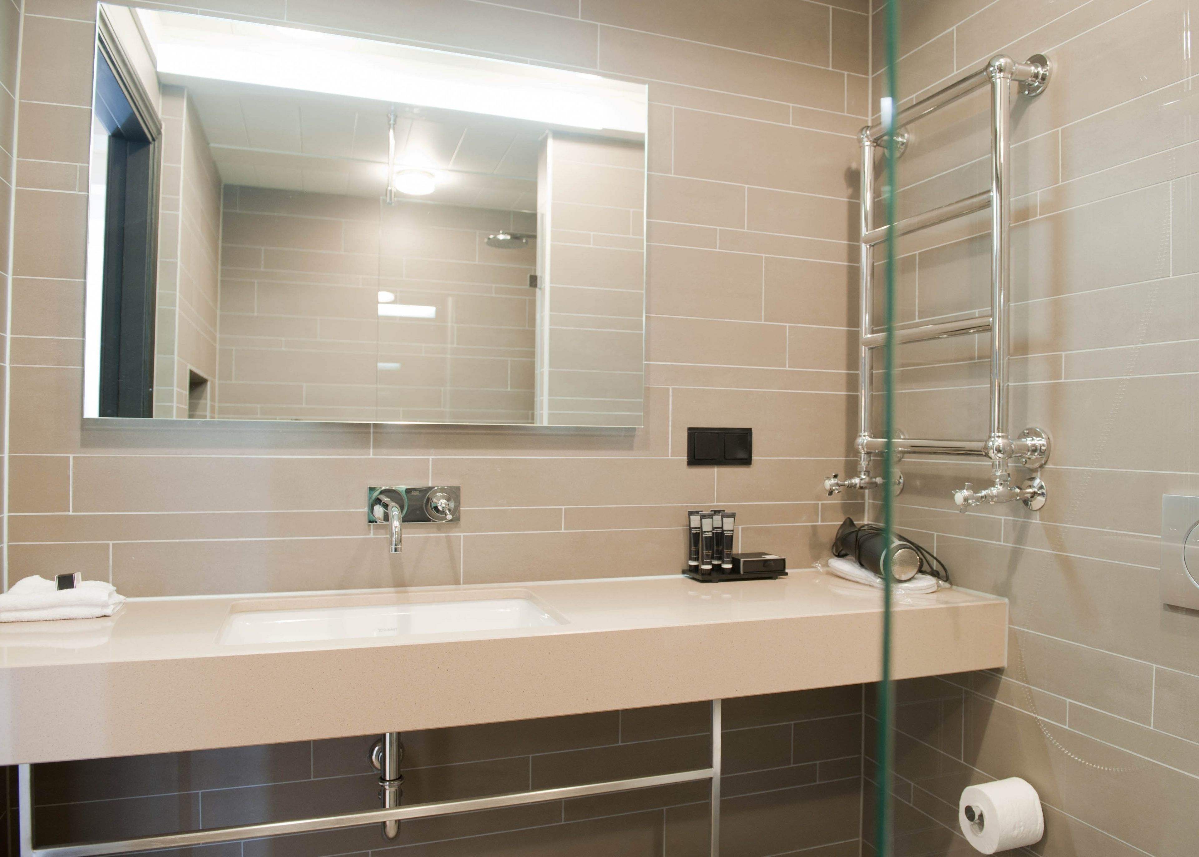 A modern bathroom with a large mirror, a sink, and a glass shower enclosure.